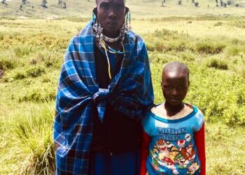 a Maasai father in traditional apparel standing with his daughter wearing western clothing