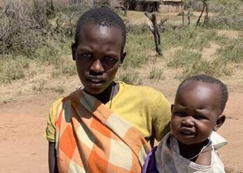 a Maasai woman holding a baby in Tanzania in front of their boma.