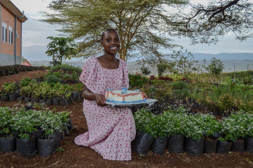 the importance of birthdays at MGRC. Maasai girl sits among flowers holding her cake.