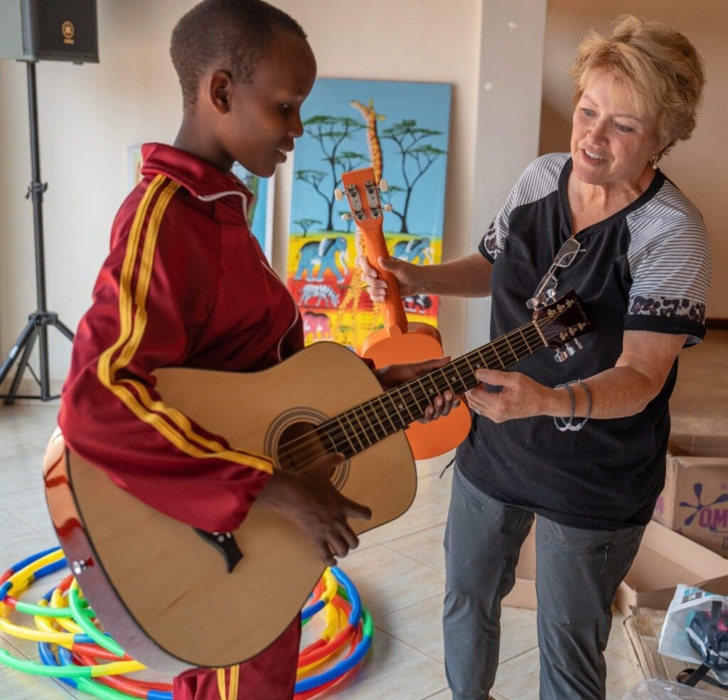 volunteers drive success.  a sponsor teaching a girl to play guitar