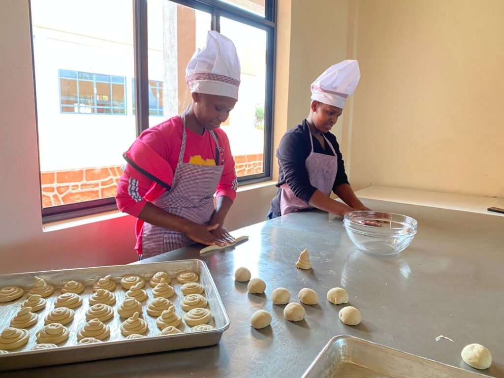 Two maasai girls rolling out dough in the kitchen an aspect of of sustainable strategy.