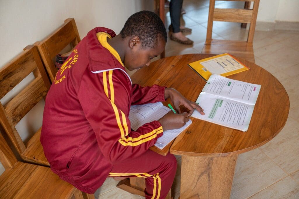 mgrc girl sitting at a table studying and doing homework. showing mgrc is a different kind african charity.