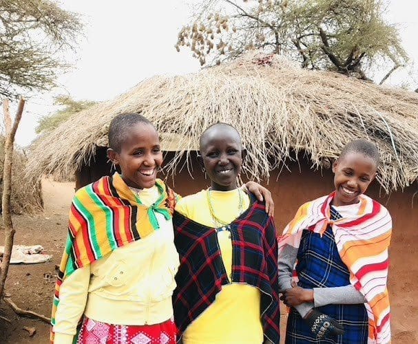 Maasai girls standing in front of a boma, highlighting the cultural and purposeful travel experience.