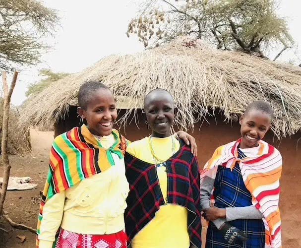 Empowering Maasai girls standing in front of a boma, highlighting the cultural and purposeful travel experience.