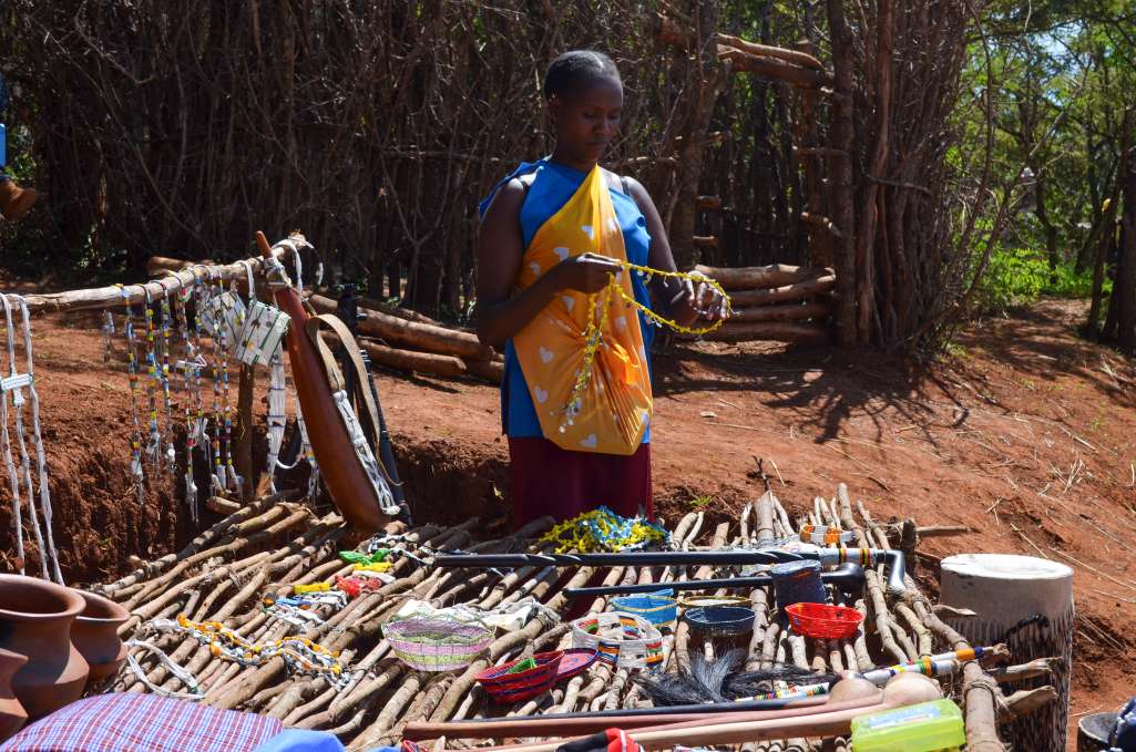 maasai woman holding beadwork in front of a display of traditional beadworks