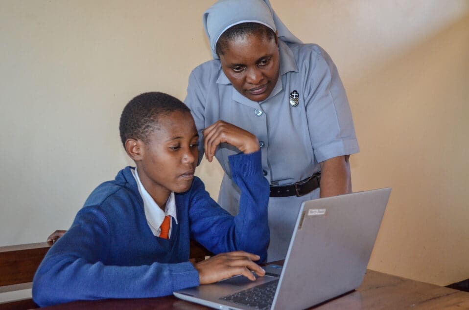 Sister Silvia leaning over to help student with laptop.