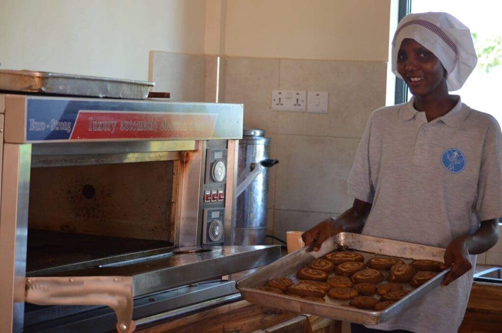 maasai young woman holding tray of baked goods pulled out of the oven 